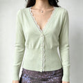 Model wearing pale mint green cropped knit cardigan, white lace trim at V-neck, fitted rib waist, long sleeves