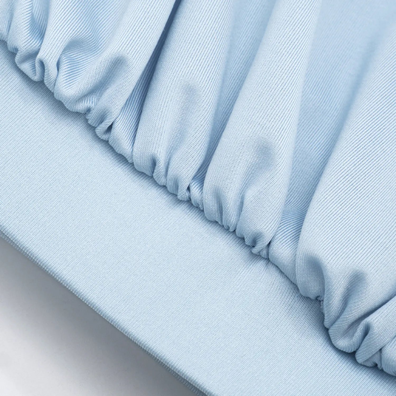 Macro close shot of wrap surplice front ruching detail, sky blue stretch knit fabric with uniform tight gathers, seamless transition to solid elastic waist band, smooth matte jersey texture