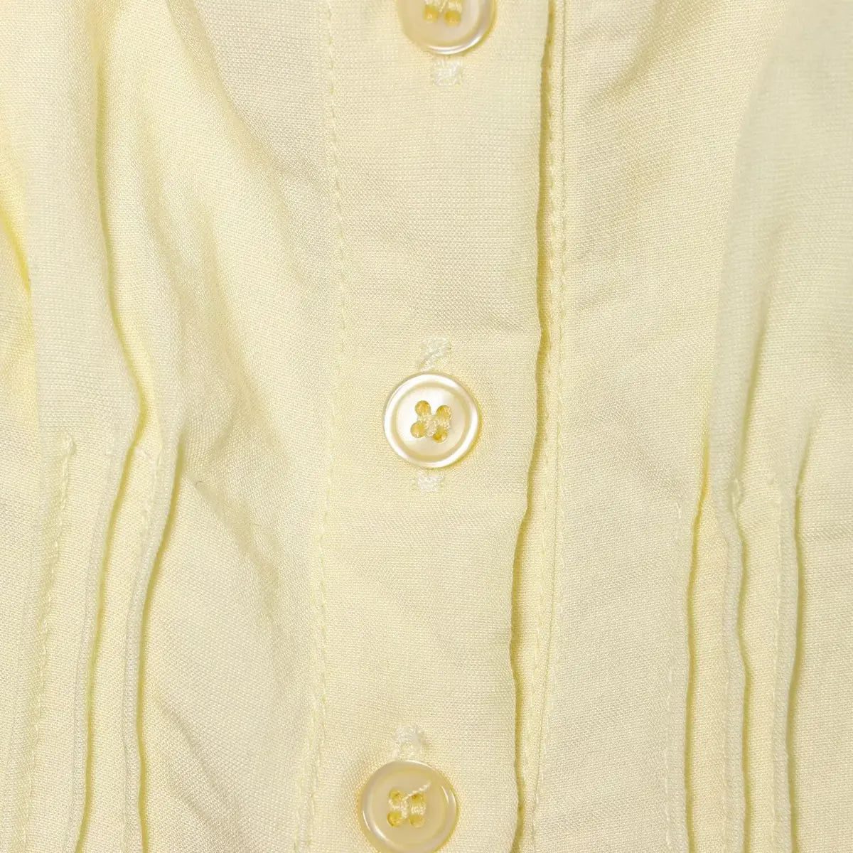 Close-up of the mother-of-pearl buttons on the pale yellow cami top, showing the stitching and fabric texture