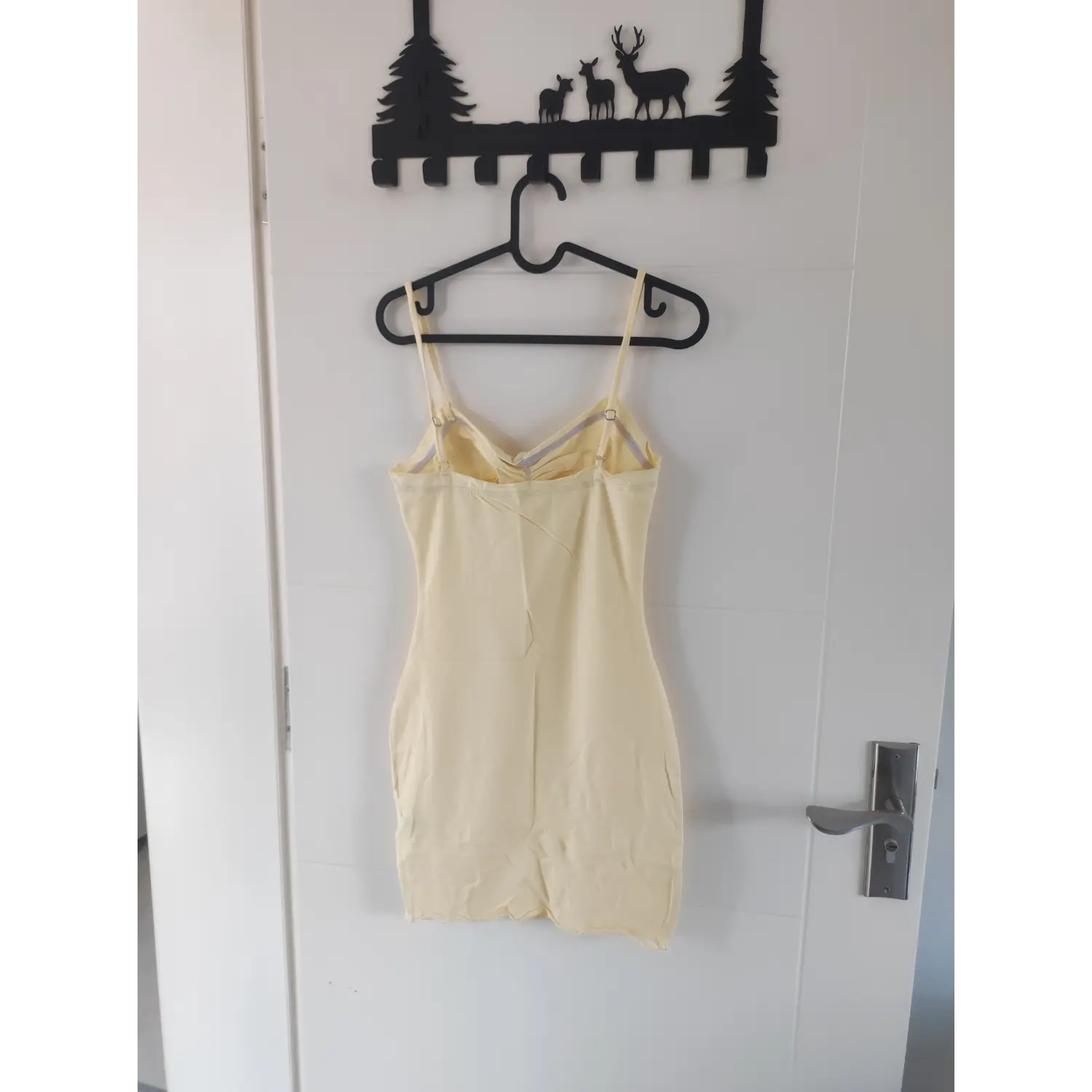 Back view of light yellow thin strap mini dress, adjustable shoulder straps hanging on hanger