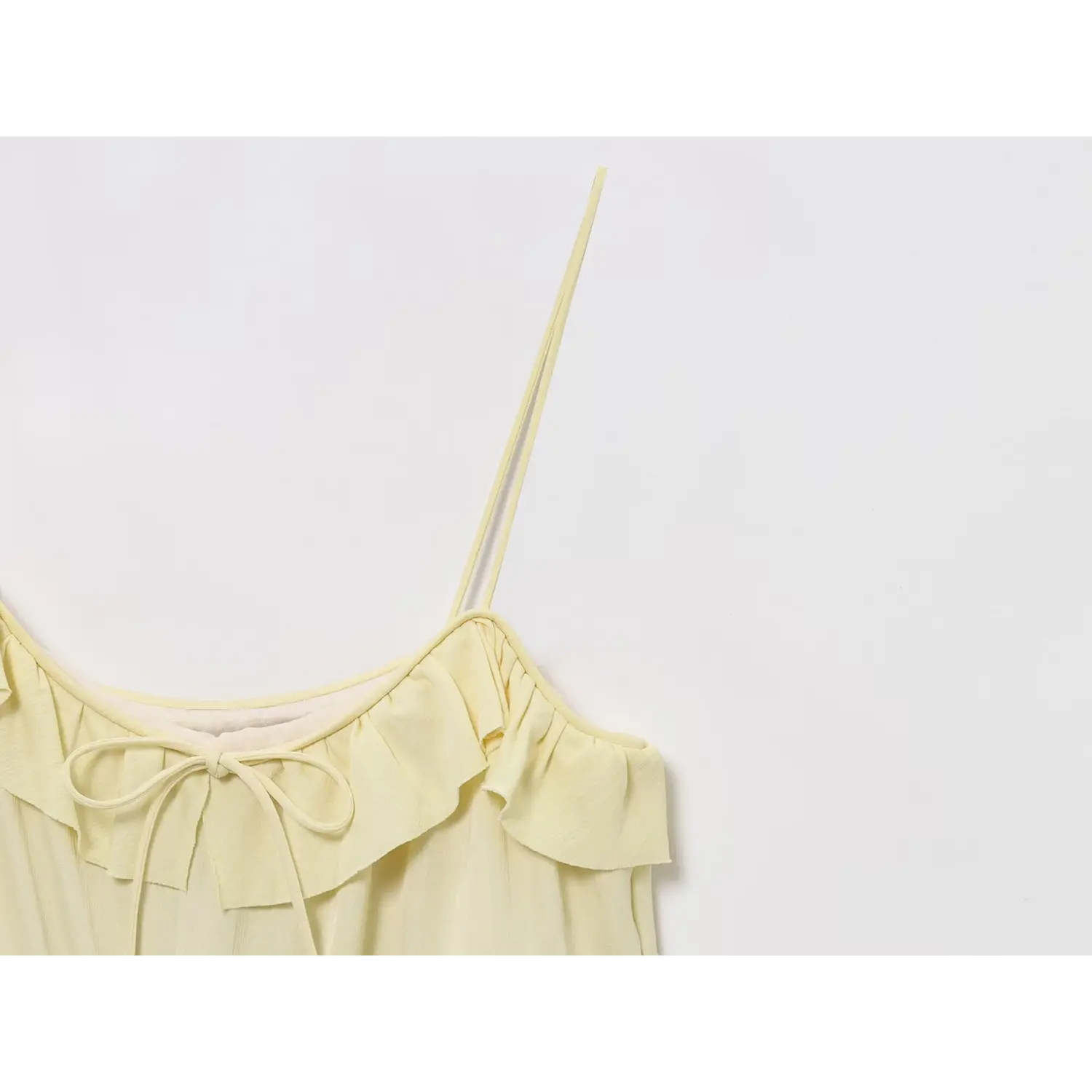 Close-up of thin spaghetti strap and ruffled neck bow on pale yellow flowy mini dress