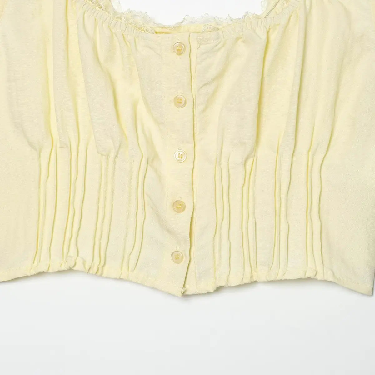 Close-up of the front button placket on the pale yellow cami top, showing the buttons and vertical pleats