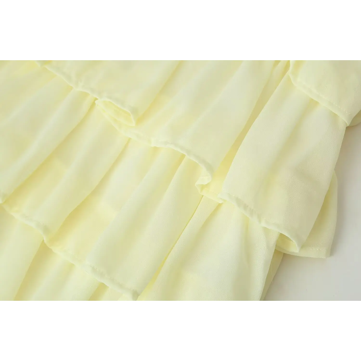 Close-up of layered tiered ruffle fabric and neat stitching on pale yellow chiffon mini skirt