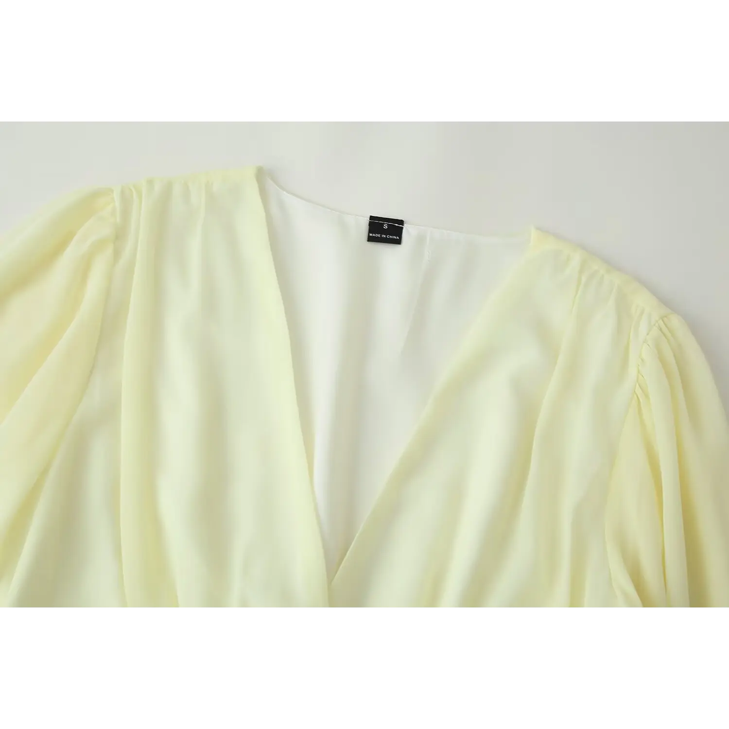 Close-up of deep v neckline and inner size label on pale yellow chiffon dress, gathered shoulder detail