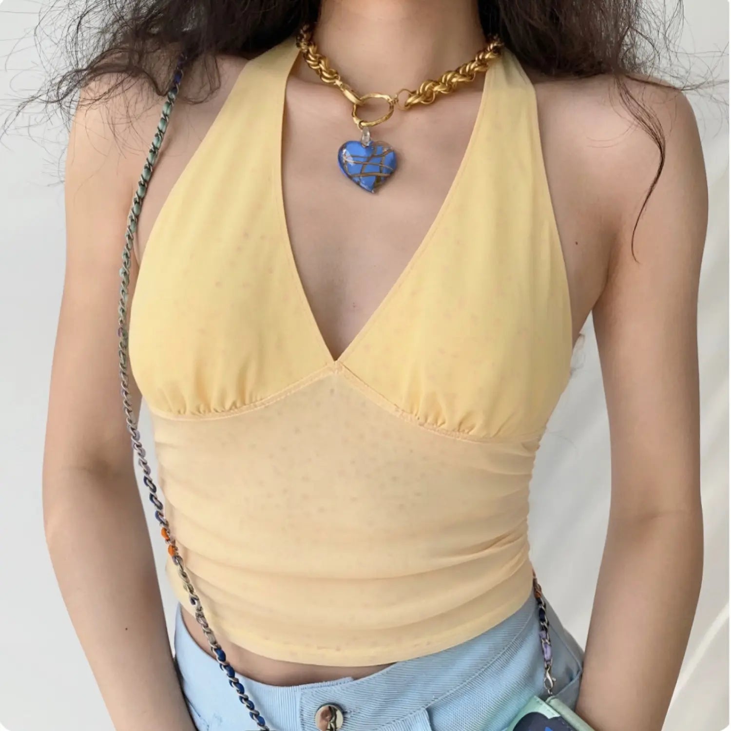 Front lifestyle shot on model, pale yellow sheer dot mesh halter V-neck tank top, gathered bust, ruched fitted waist, cropped length, matched with light blue denim bottoms and necklace, casual sweet daily outfit