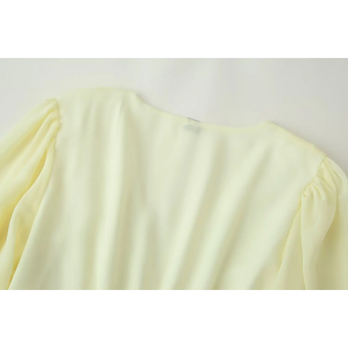 Back neck and gathered shoulder close-up of pale yellow chiffon mini dress, smooth fabric texture