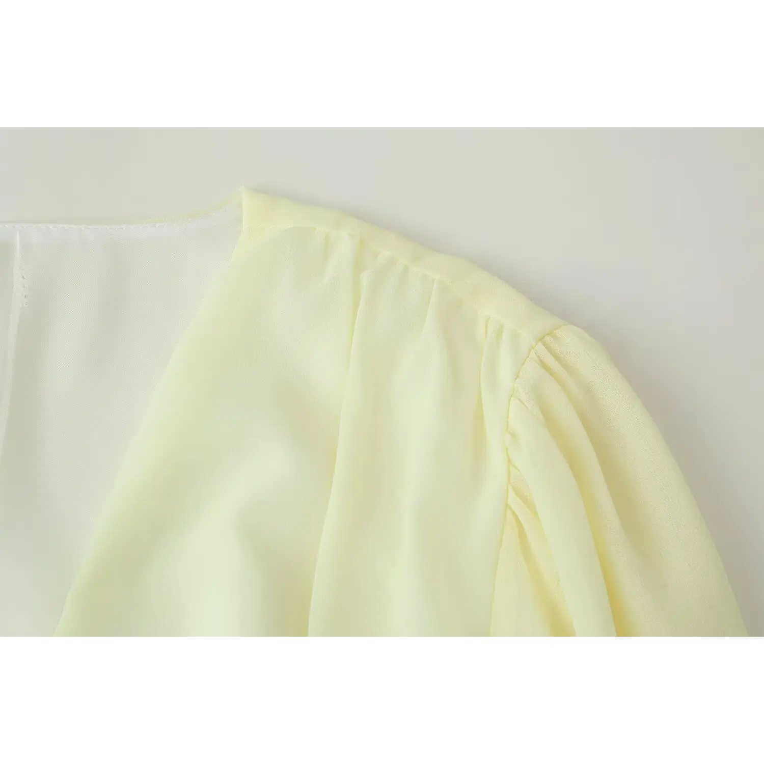 Macro shot of gathered shoulder and sleeve construction on pale yellow chiffon ruffle mini dress