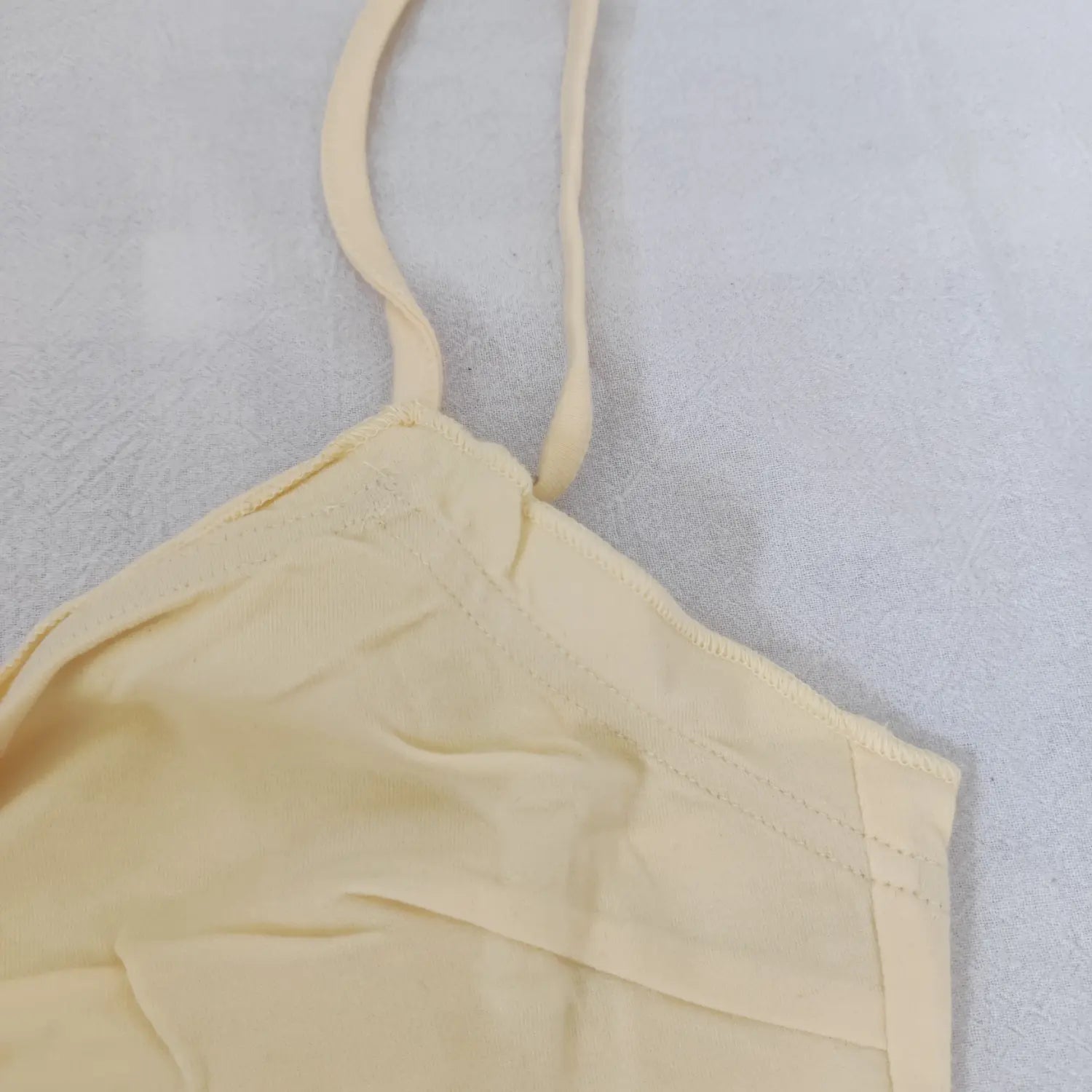 Close up of adjustable thin strap stitching on light yellow cami dress