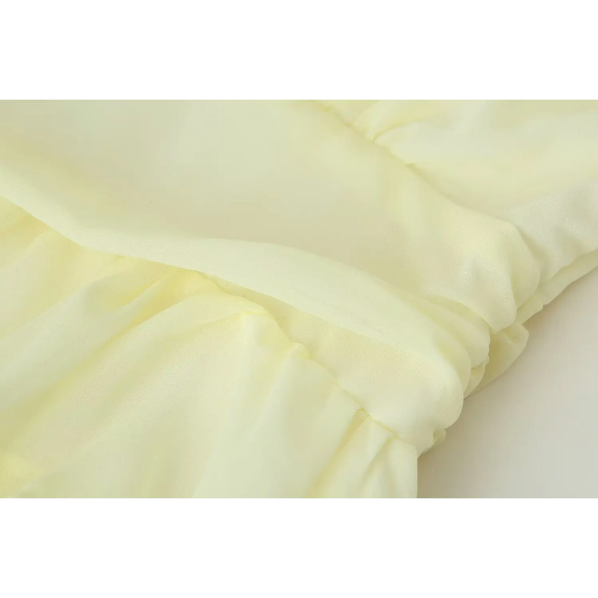 Close view of waist ruffle connection and lightweight chiffon material for pale yellow tiered dress