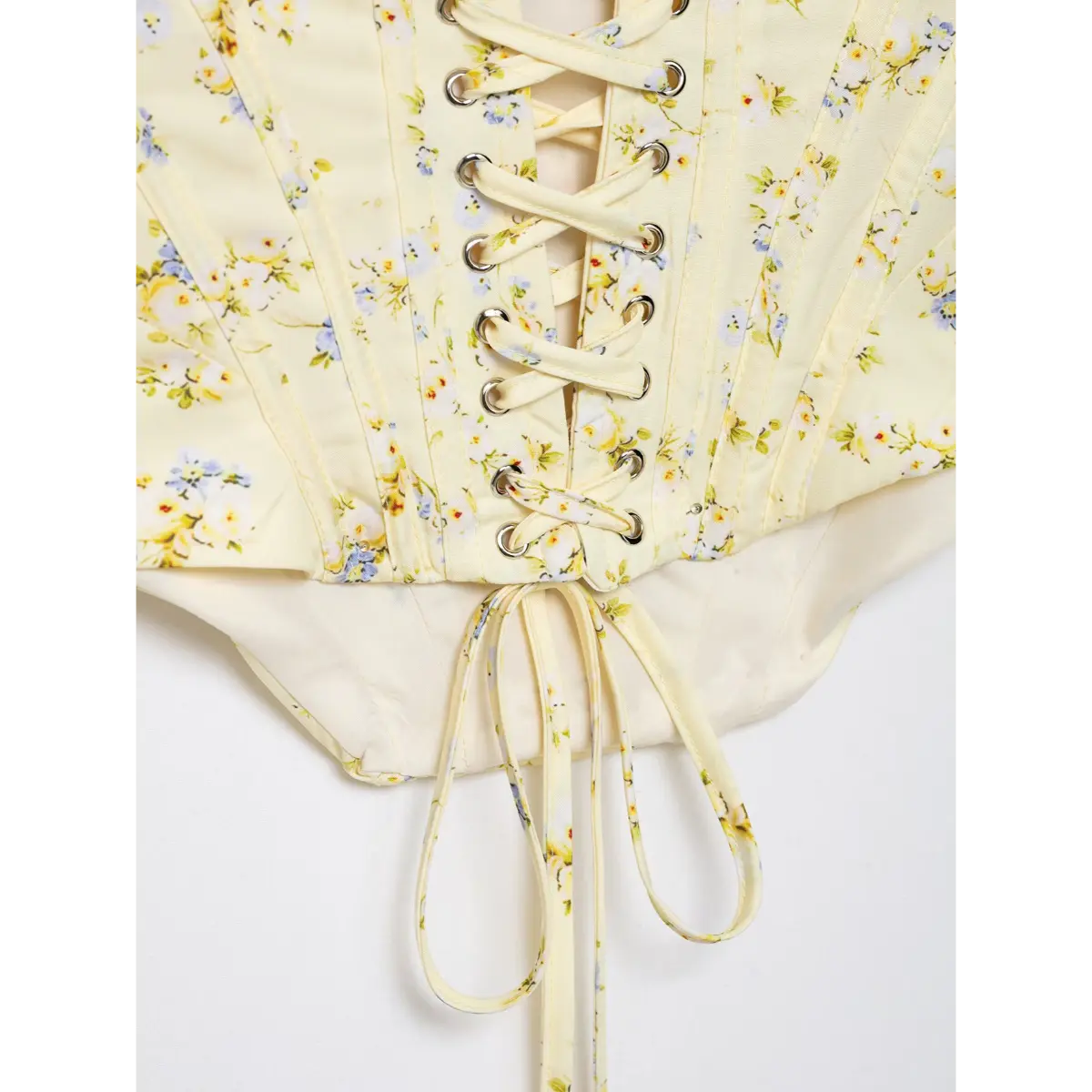 Close-up view of crisscross lace-up closure on the back of pale yellow floral print corset top with lace trim.