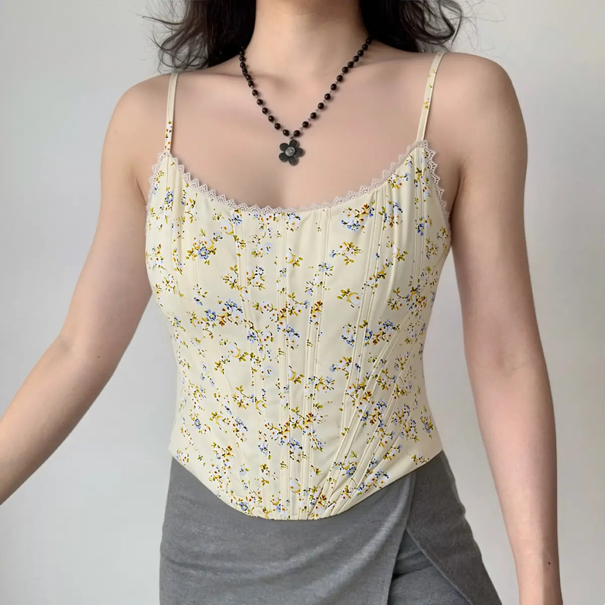 Full body shot of a woman wearing pale yellow floral lace corset top matched with grey bottoms.
