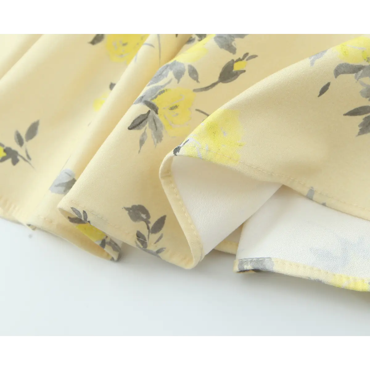Close-up of the fabric lining and hem stitching on a pale yellow floral print spaghetti strap dress.