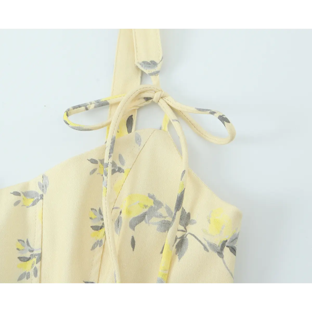 Close-up of the adjustable tie closure on the spaghetti strap of a pale yellow floral print dress.