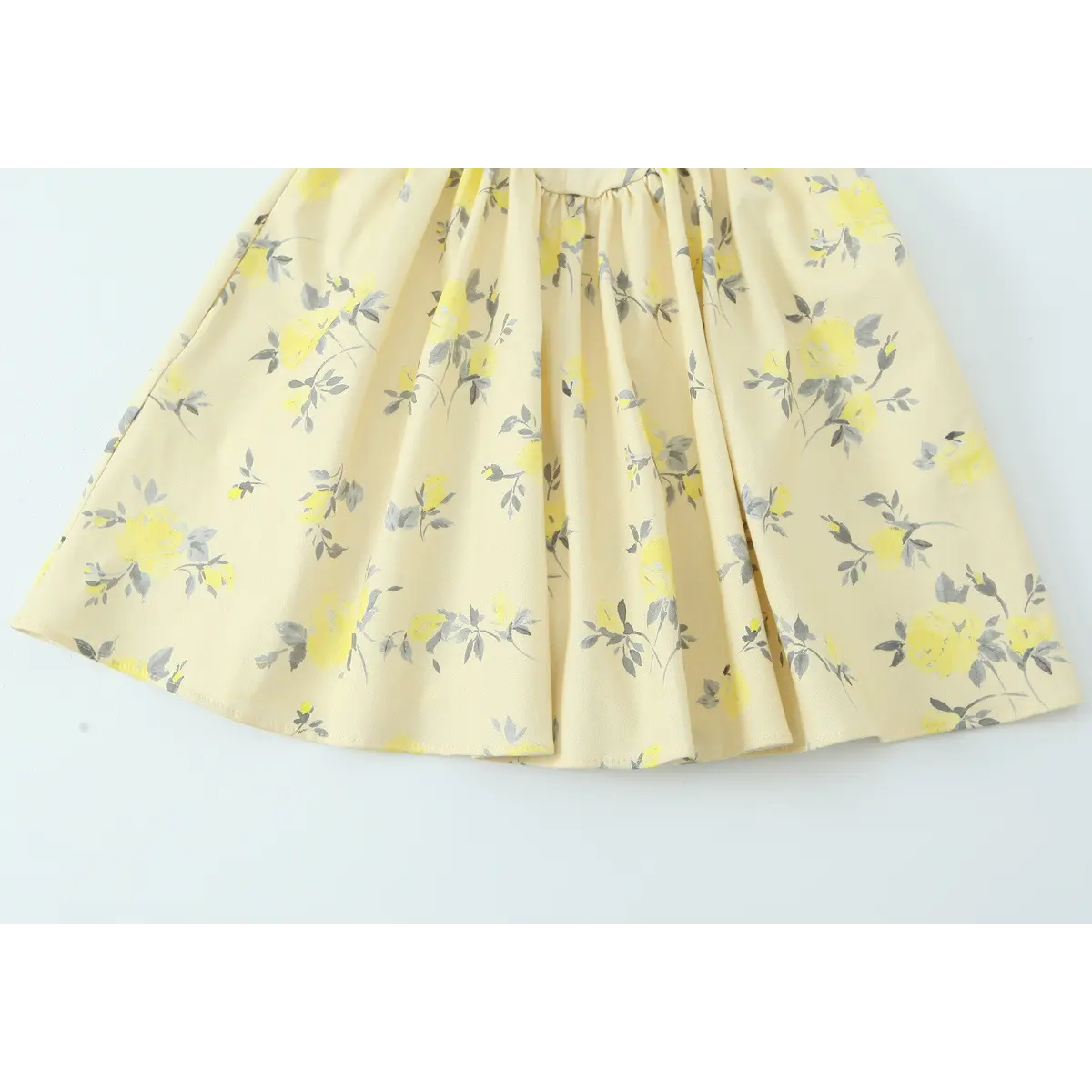 Close-up of the gathered skirt hem on a pale yellow floral print spaghetti strap dress, displaying the flowy silhouette.
