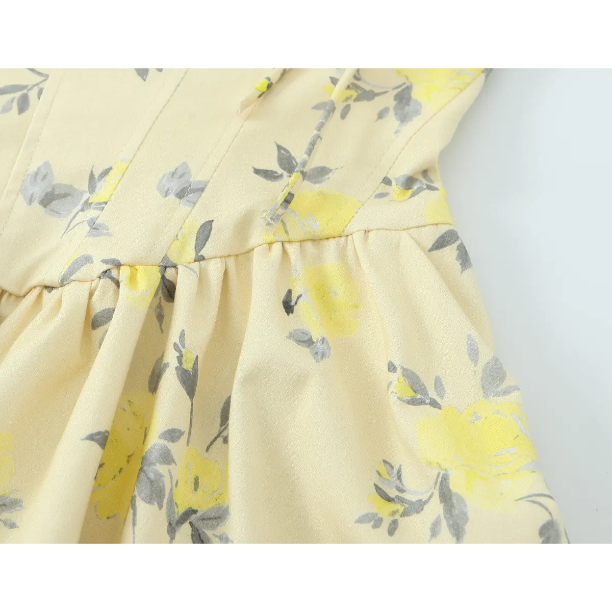 Close-up of the waist seam where the bodice meets the gathered skirt on a pale yellow floral print dress.
