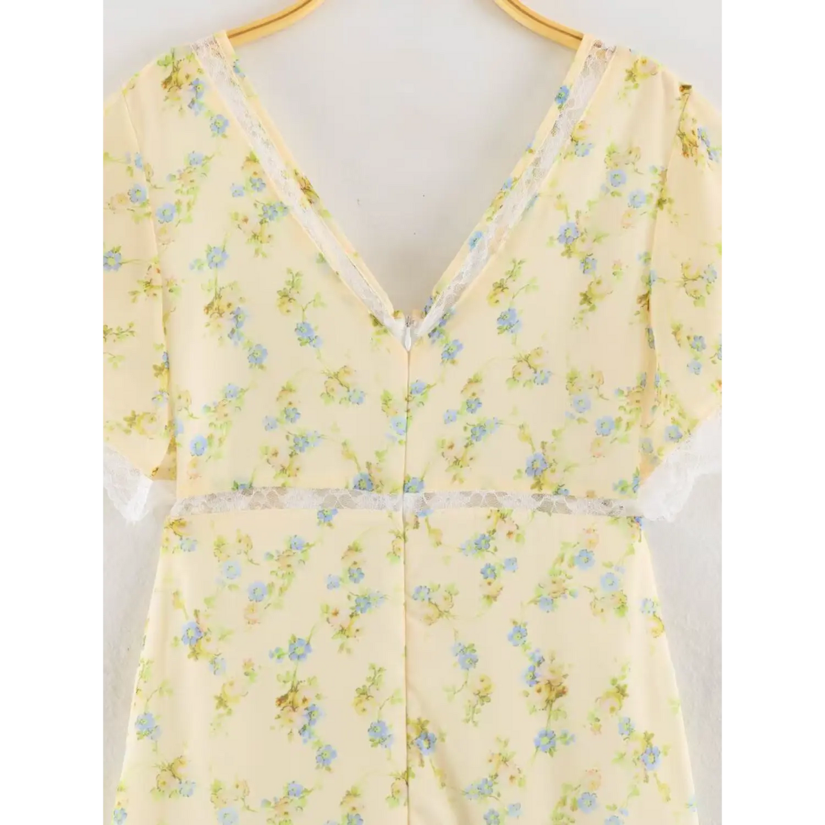 Hanging back view of pale yellow floral maxi dress upper torso, deep V back trimmed with delicate white lace, central invisible zipper