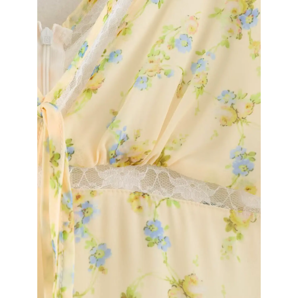 Close-up of the bust part on pale yellow floral maxi dress, white lace trim along neckline and waist, matching fabric front tie