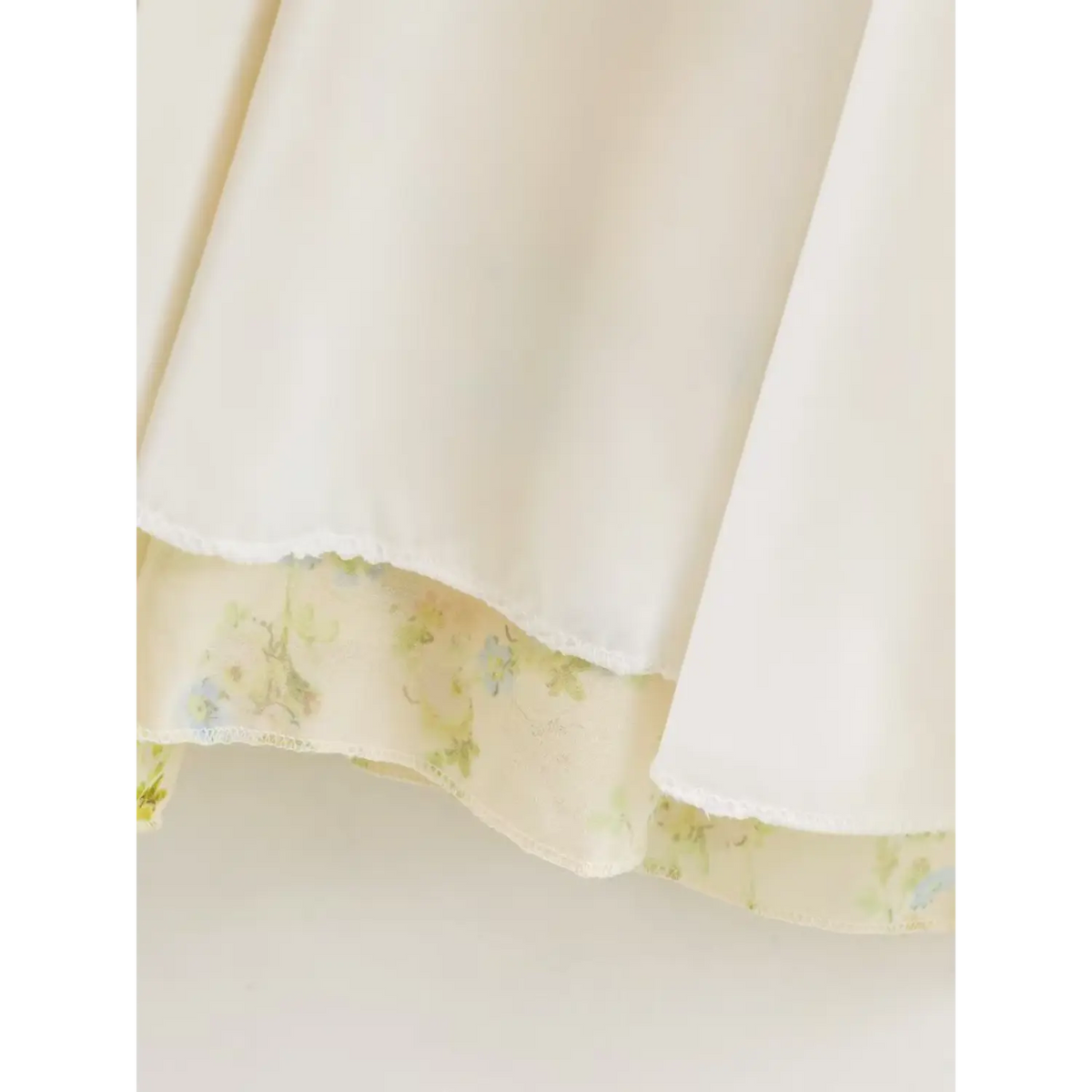 Macro detail of pale yellow floral maxi dress hem, showing neat stitching of white lining and translucent floral chiffon outer layer
