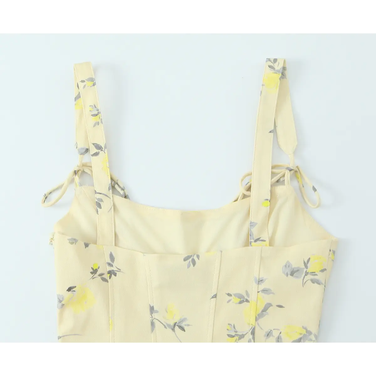 Close-up of the back view of a pale yellow floral print spaghetti strap dress, showing the tie straps and structured bodice.