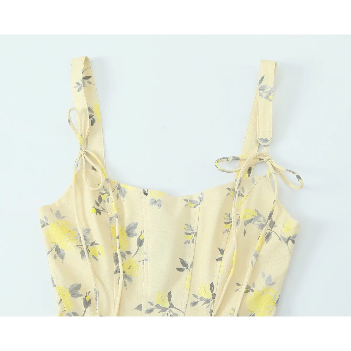 Close-up of the front bodice, tie straps, and floral print on a pale yellow spaghetti strap dress.