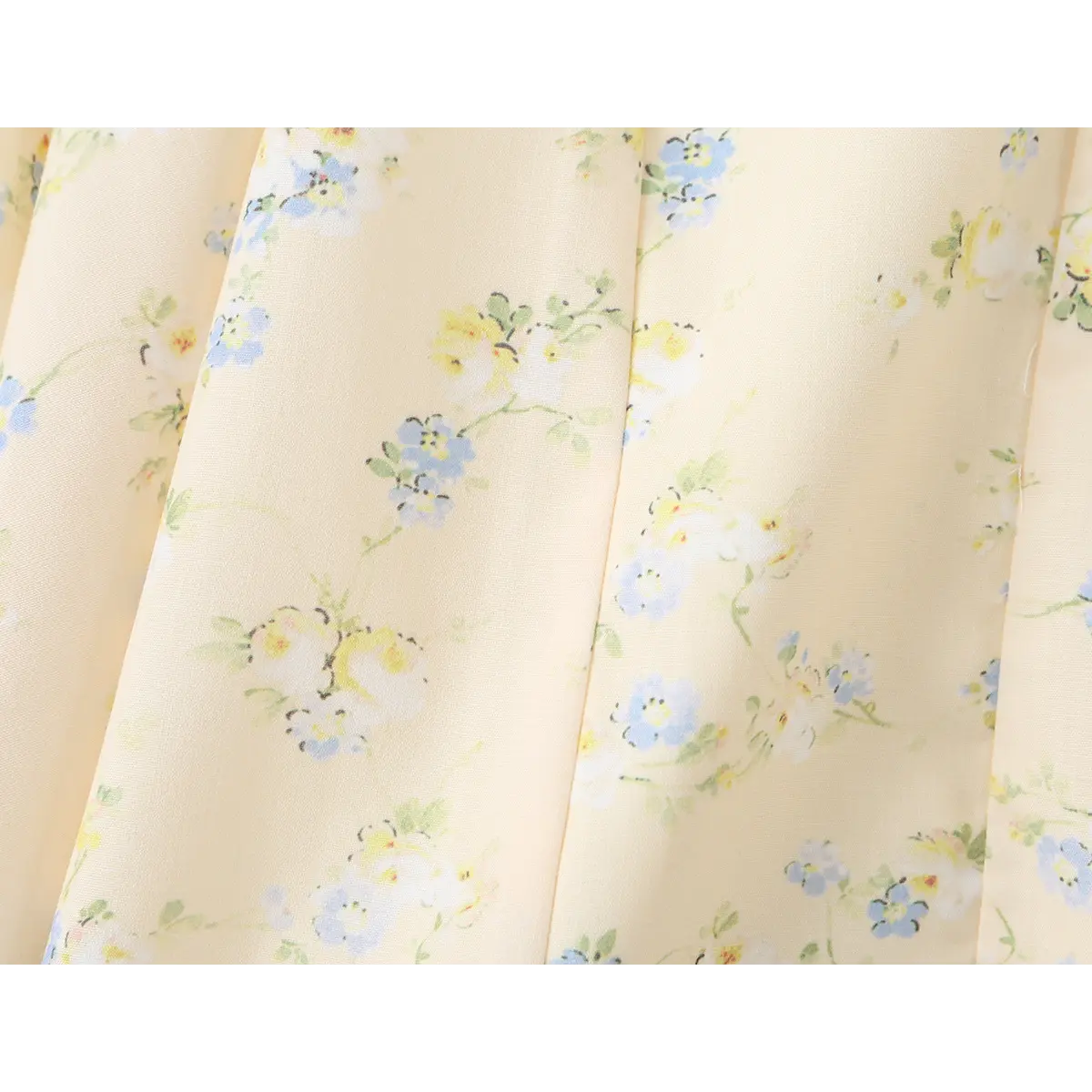 Close-up of the ditsy floral print, featuring blue and yellow flowers on a pale yellow background.