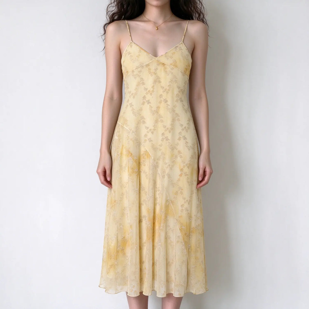Model wearing pale yellow floral spaghetti strap maxi dress, flowy chiffon fabric, v neck, asymmetrical panel design, white background