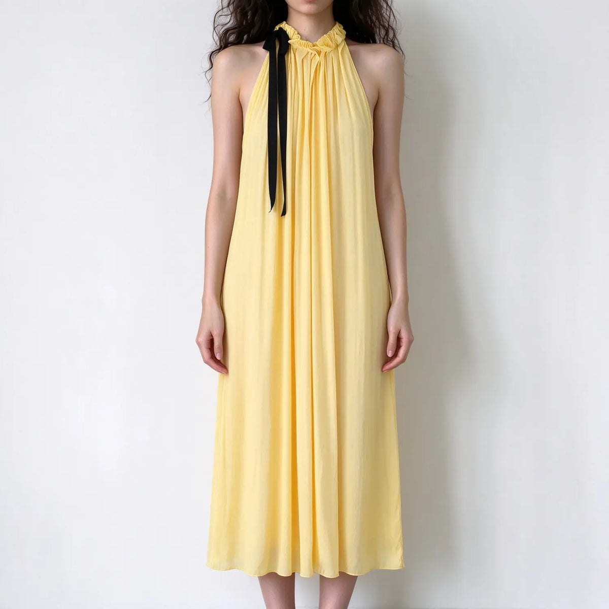 Model wearing pale yellow halter maxi dress with black ribbon tie at neck, loose flowy silhouette, solid color, white background