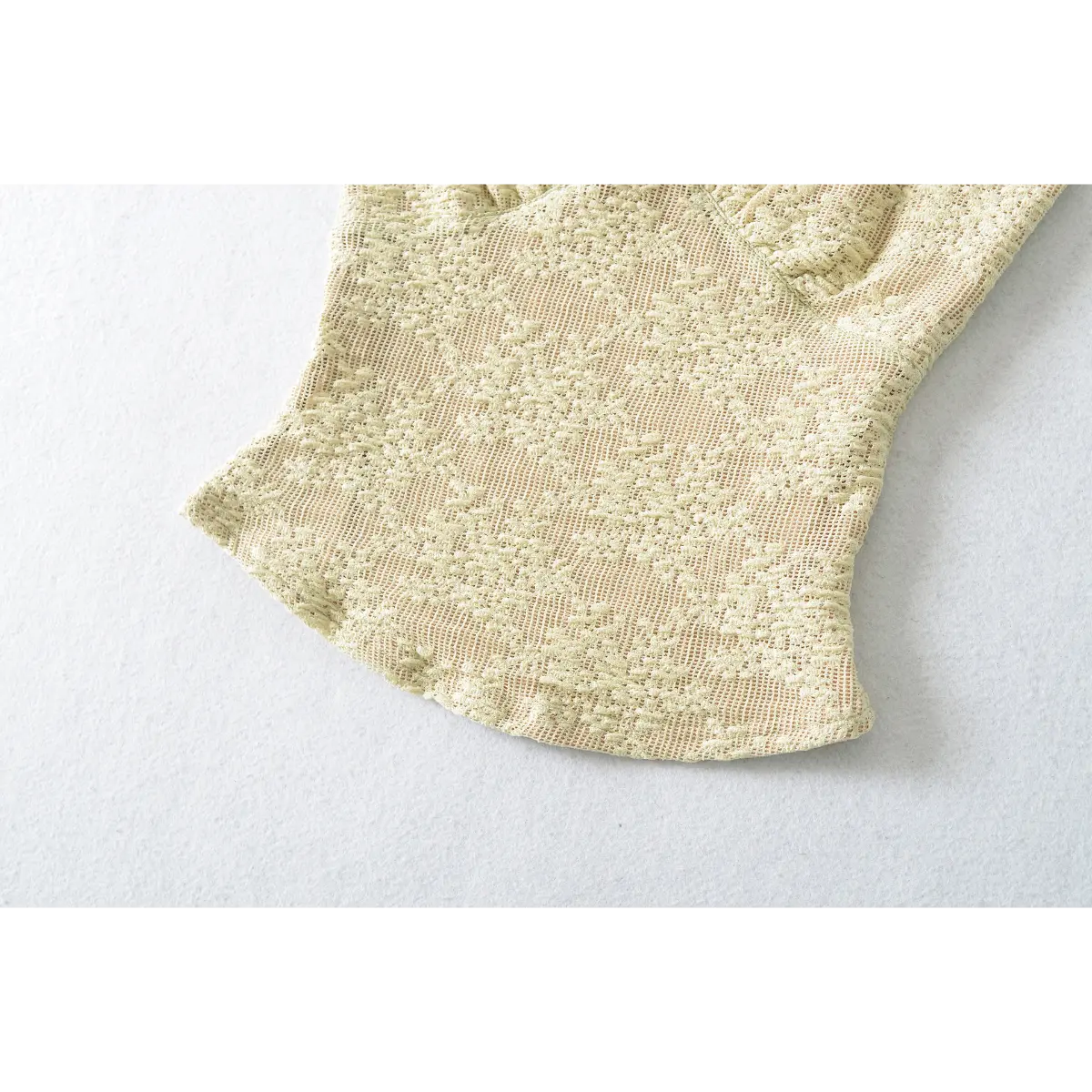Close-up of the curved hem on the pale yellow lace camisole, showing the detailed pattern.