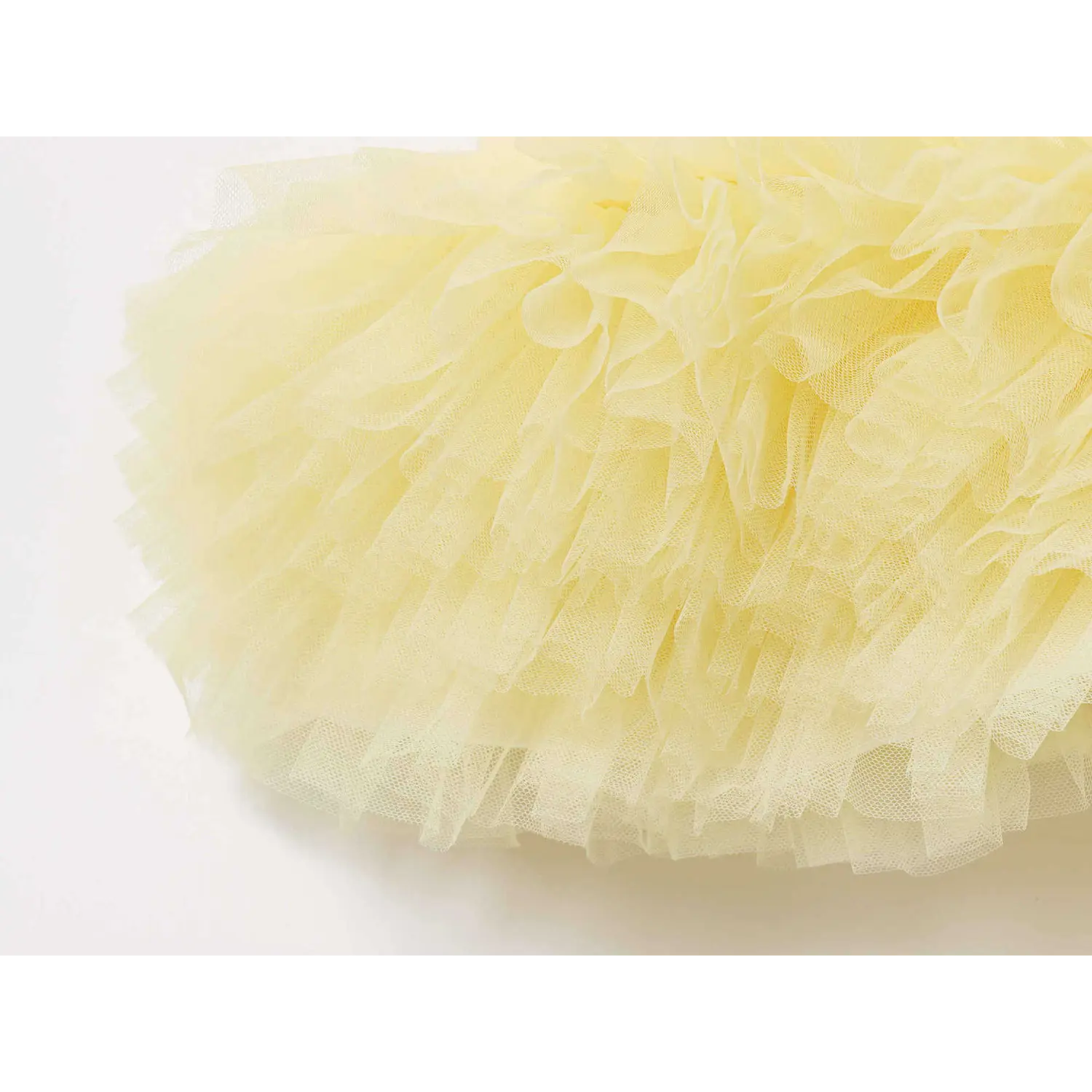 Extreme close-up of layered ruffled pale yellow tulle fabric hem on cami peplum