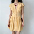 Model wearing a pale yellow short-sleeve mini dress with a deep V-neck, cinched waist, and front button placket leading to a flared skirt.