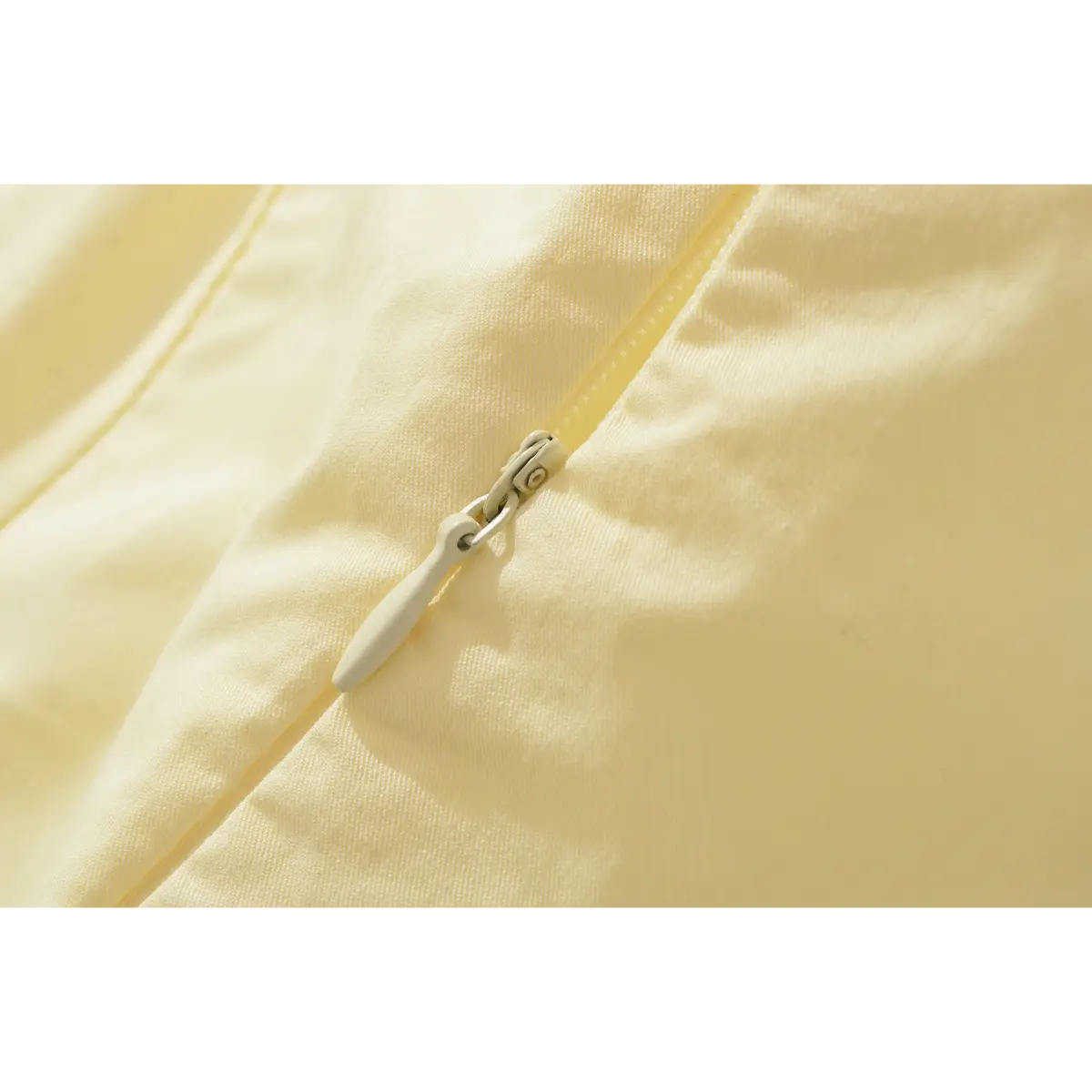 Close-up of the pale yellow dress's back zipper, showing the light-colored pull tab and fine fabric texture.