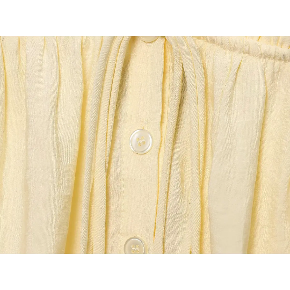 Close-up of the shell buttons and front tie detail on the pale yellow camisole top.