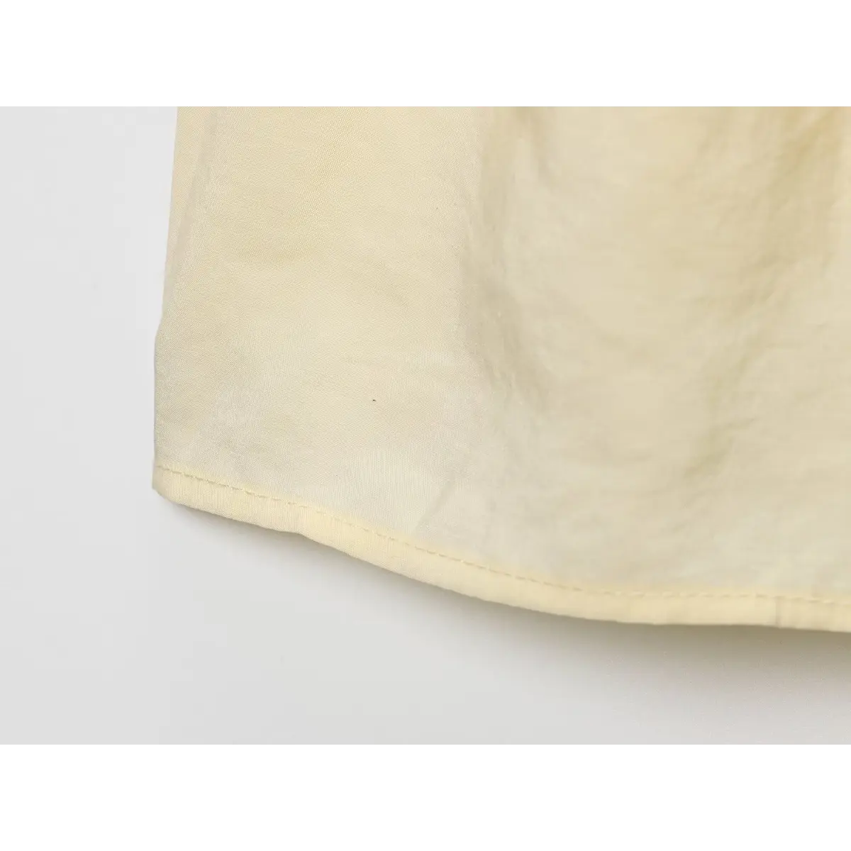 Close-up of the neatly finished bottom hem on the pale yellow camisole top.
