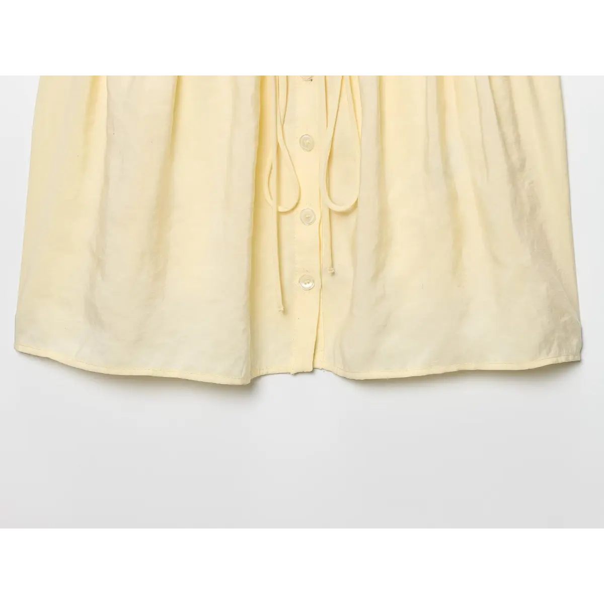 Full view of the gathered peplum hem and button placket on the pale yellow camisole.