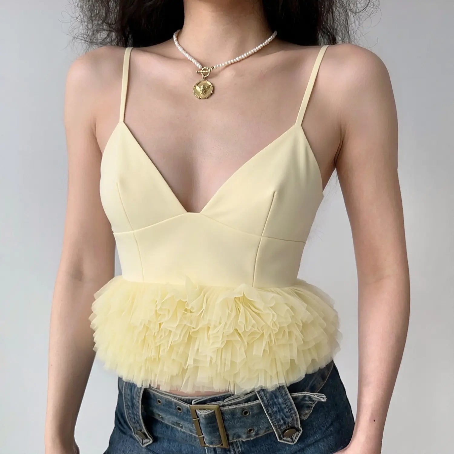 Lifestyle model photo wearing pale yellow deep V spaghetti strap camisole with layered tulle peplum