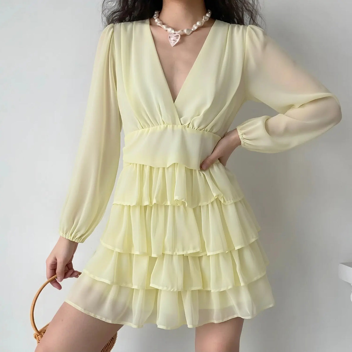 Model wearing pale yellow deep v neck chiffon mini dress, long balloon sleeves and tiered ruffle cake skirt