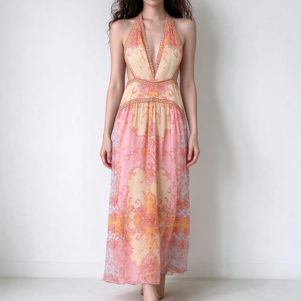 Model in boho halter maxi dress, deep v neck, side waist cutouts, pink orange vintage paisley print, flowy chiffon maxi skirt, plain white background