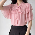 Lifestyle model outfit shot pastel pink chiffon blouse, tie bow neck, floral lace shoulder panel, tier flutter short sleeve