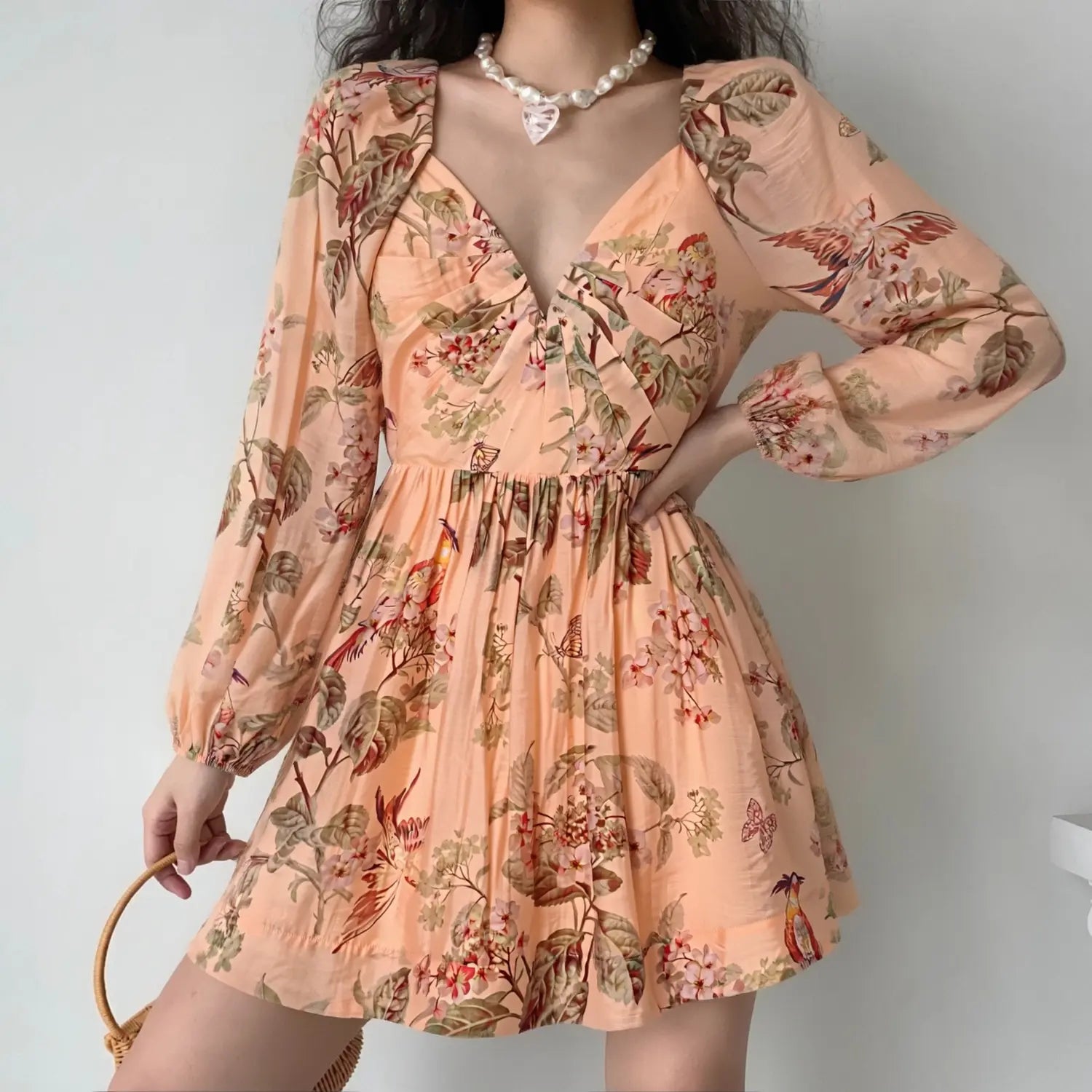 Model wearing peach vintage botanical bird print mini dress, deep v neck, long balloon sleeves, flowy babydoll short skirt