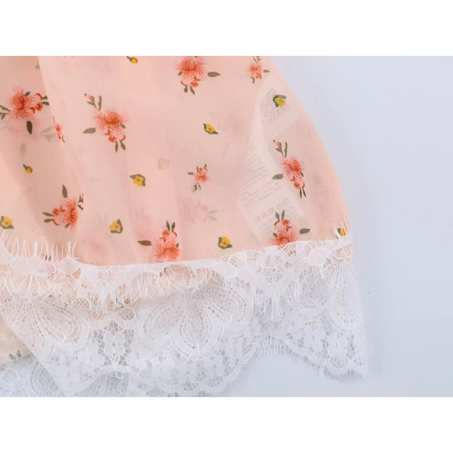 Fabric closeup small flower ditsy print, inner care label beside lace hem