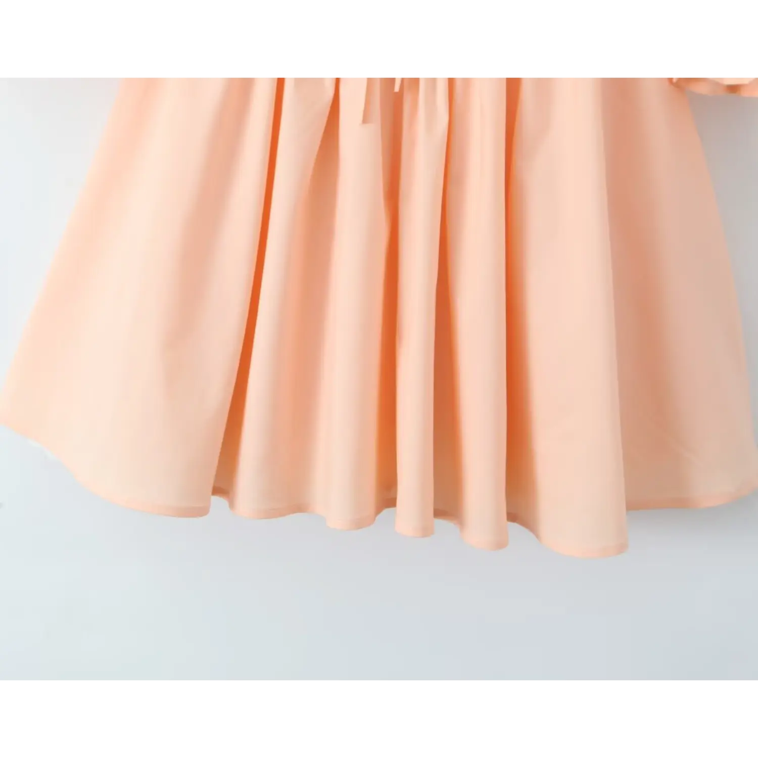 Close‑up of peach mini dress gathered flared skirt, flowy woven fabric hem detail
