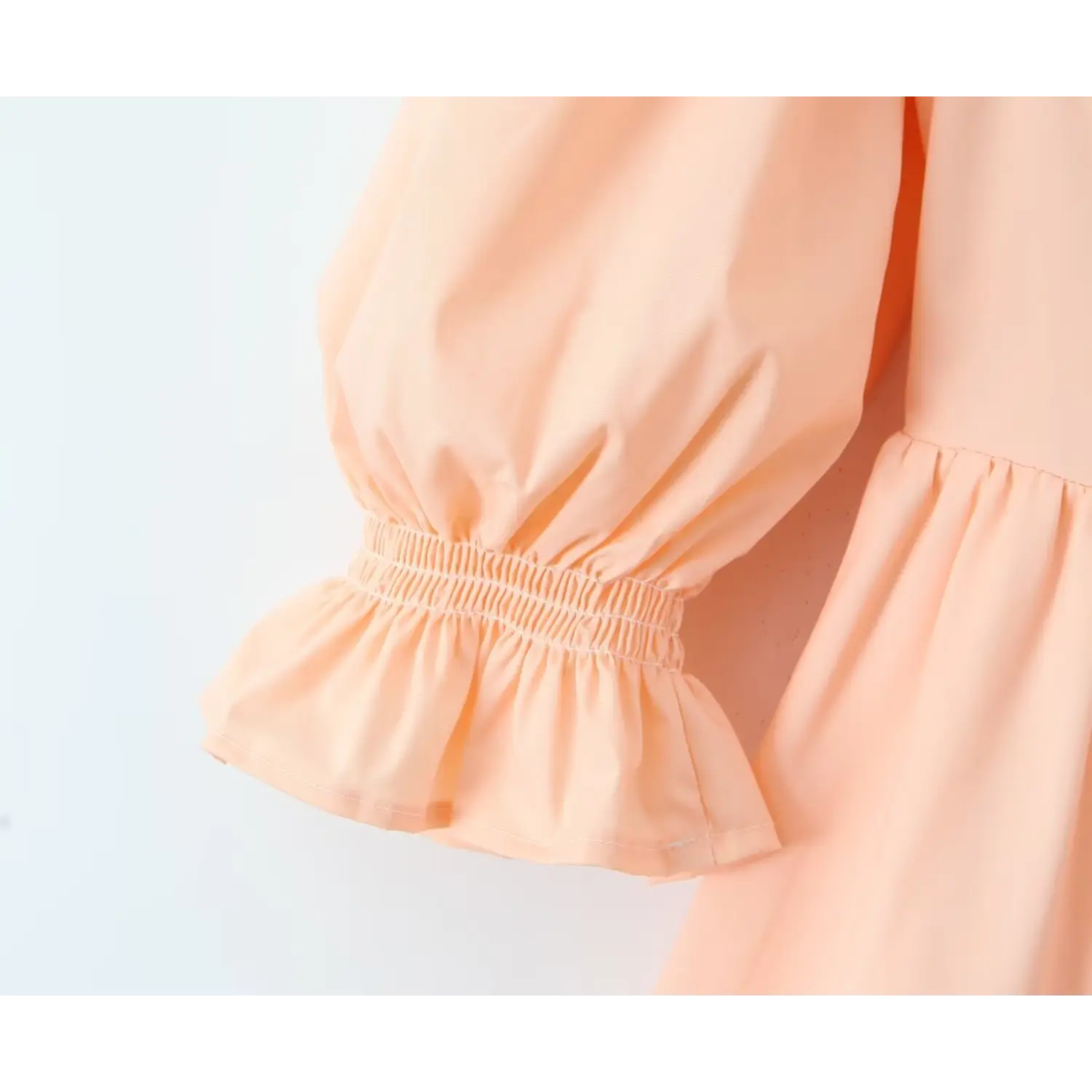Close‑up view of peach dress puff sleeve elastic ruffle cuff, smocked elastic wrist detail