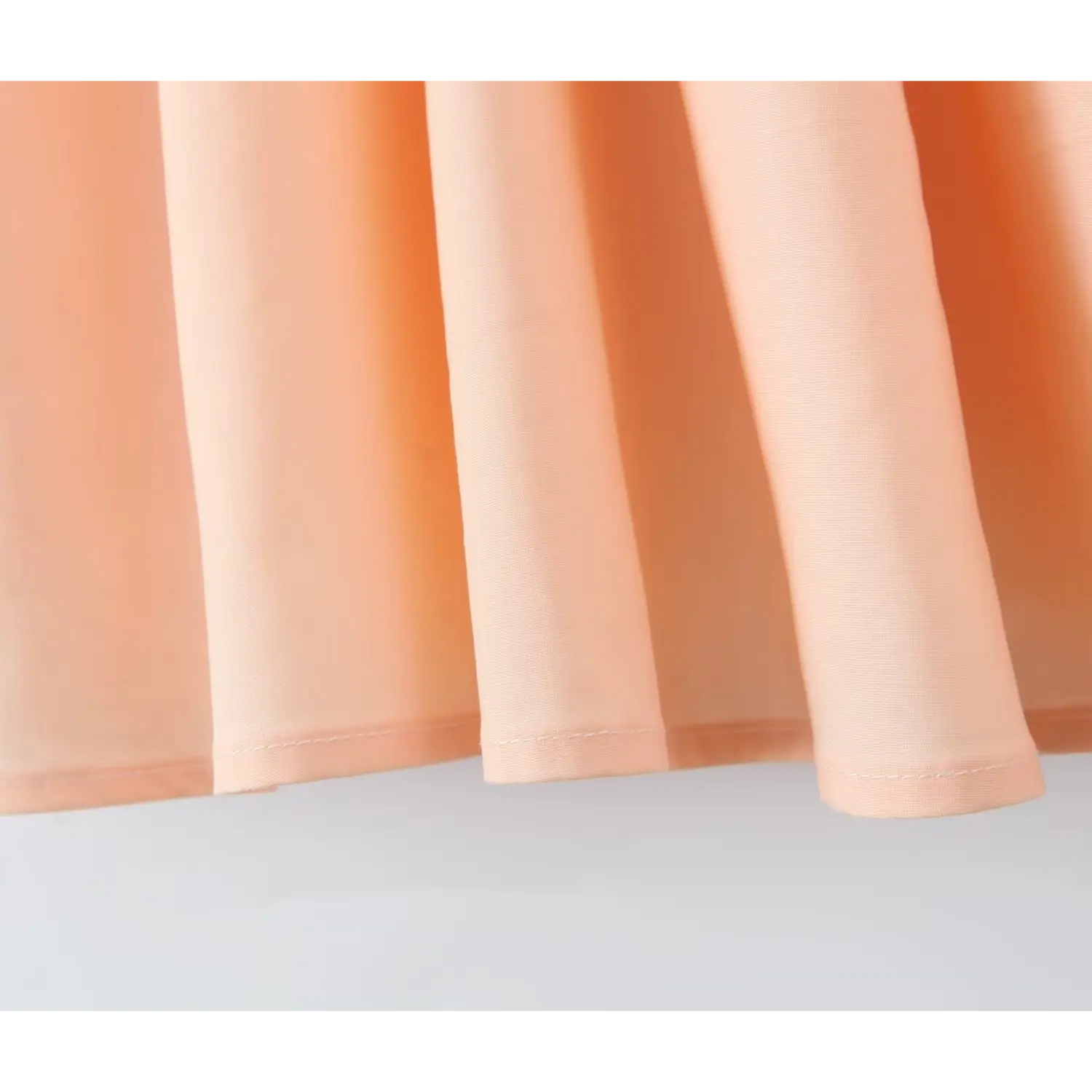 Macro close‑up of peach dress skirt finished hem, neat stitching woven fabric texture