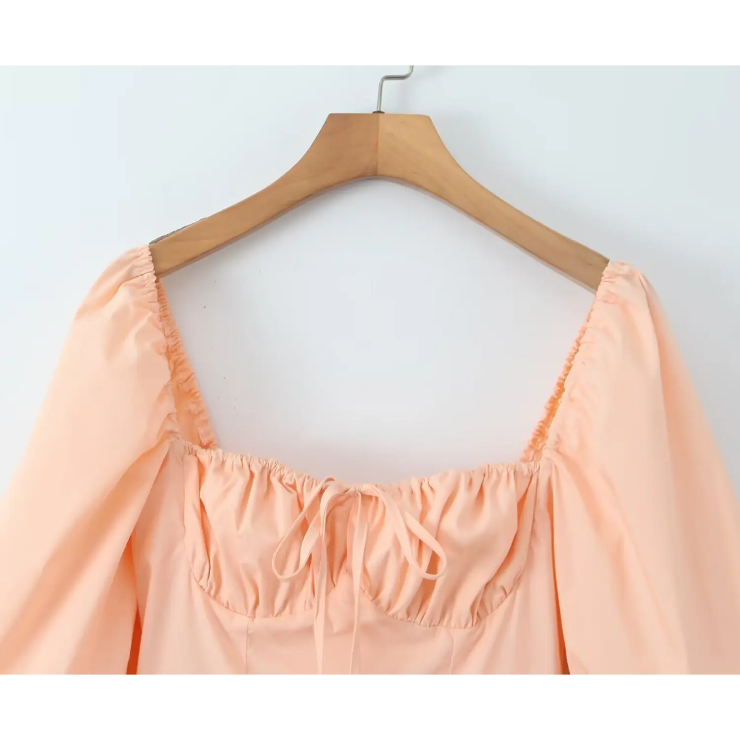 Close‑up square neckline and front tie bust detail of peach puff sleeve mini dress, gathered ruched bust design