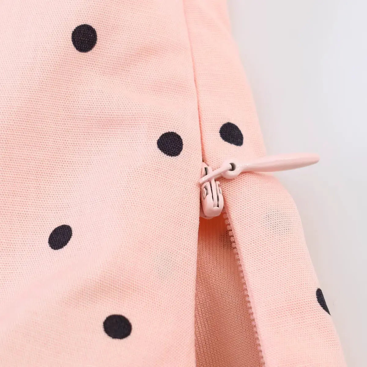 Close-up of the side zipper on the peach polka dot top, showing the matching peach-colored zipper pull