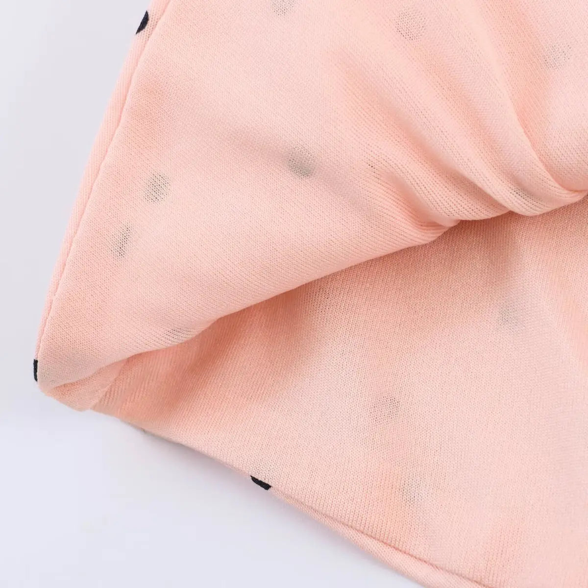 Close-up of the peach polka dot knit fabric, showing the mesh texture, black polka dots, and finished edge stitching
