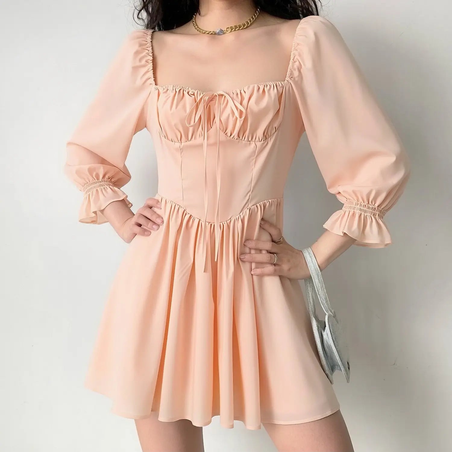 Woman model wearing peach square neck puff sleeve mini dress, tie front bust fit‑flare short dress