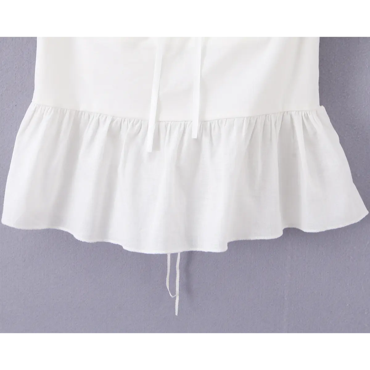 Close-up of the peplum hem on a white off-shoulder top, showing the gathered ruffled edge and smooth fabric finish.