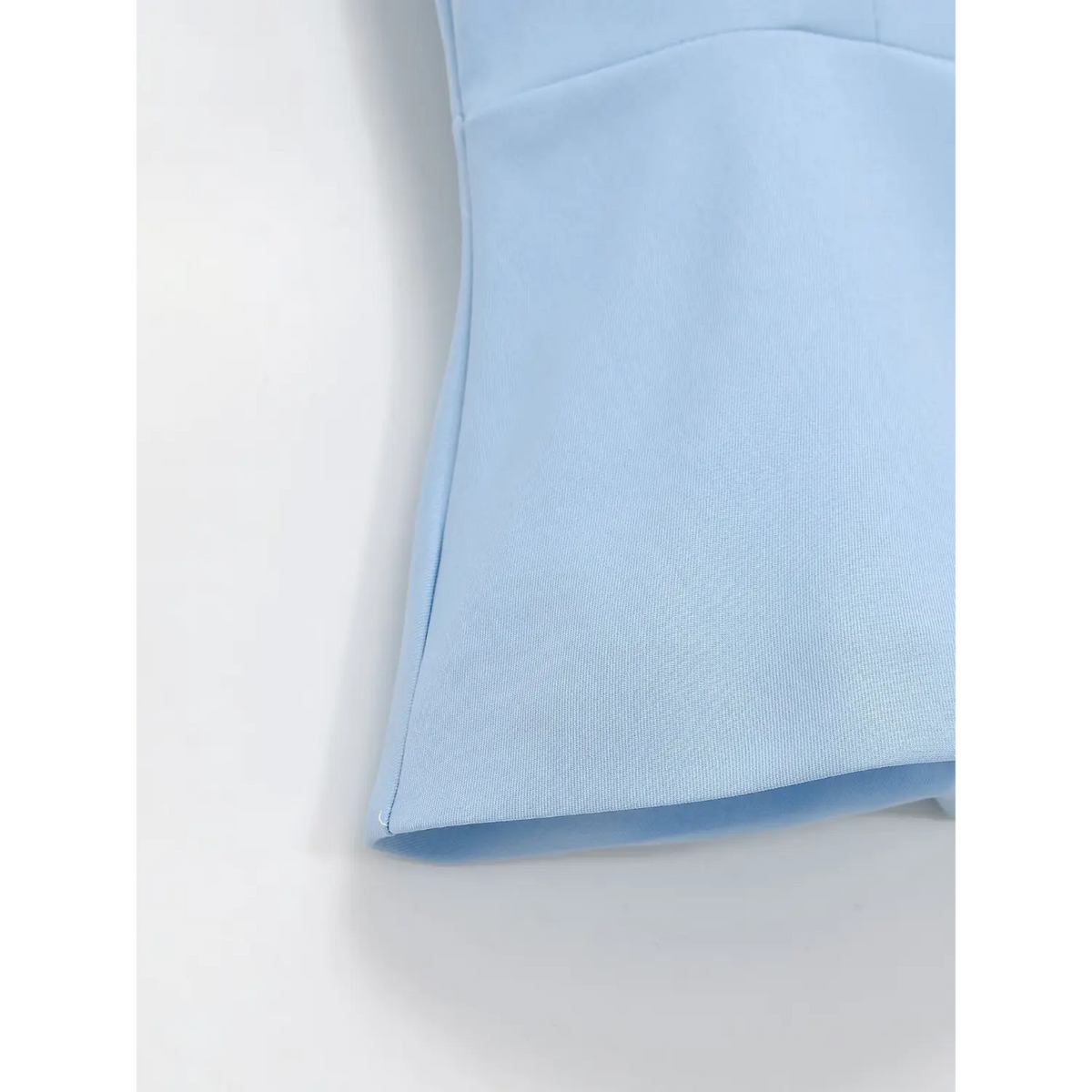 Close-up of light blue peplum vest hem, smooth woven fabric with neat stitching
