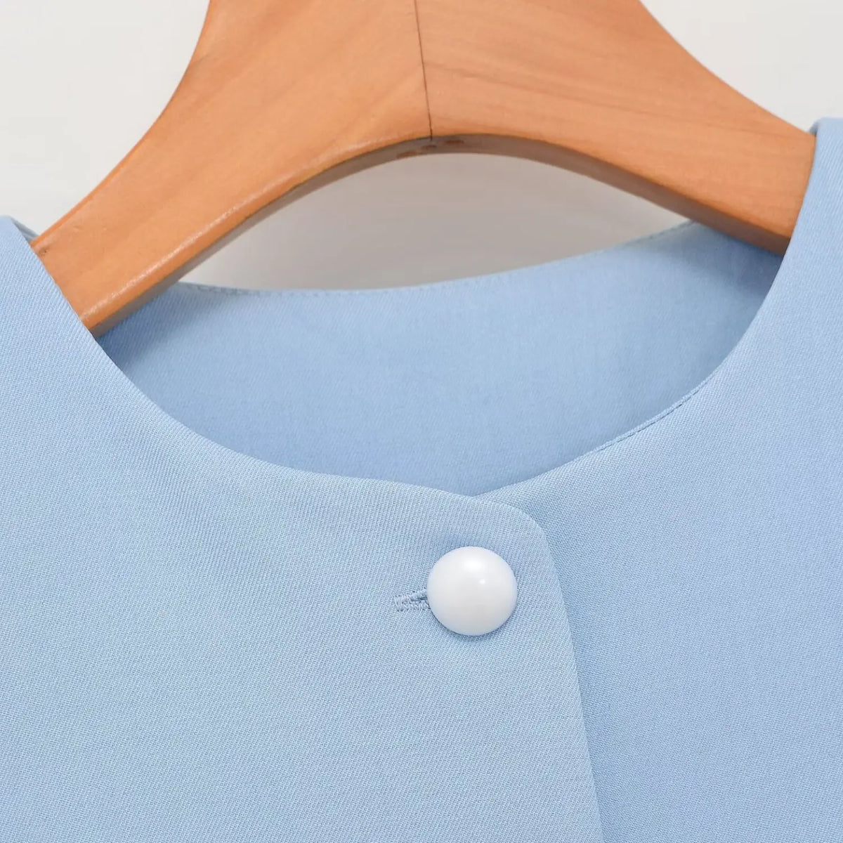Close-up shot of round neck and white pearl button on light blue tailored peplum waistcoat